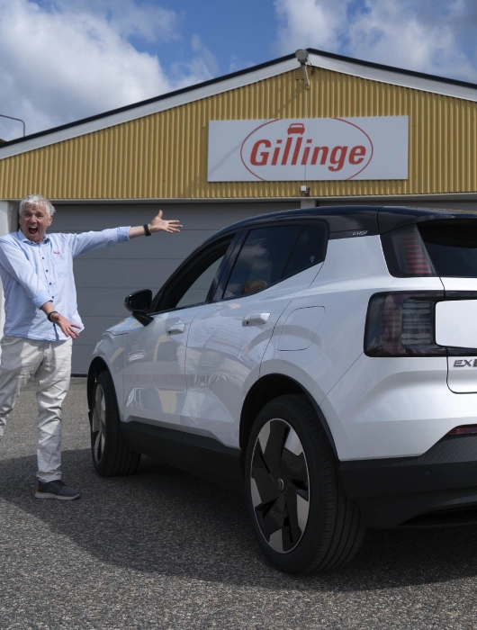 Hasse står bredvid en vit Volvo EX30 framför garaget som har Gillinges logotyp ovanför garagedörrarna.